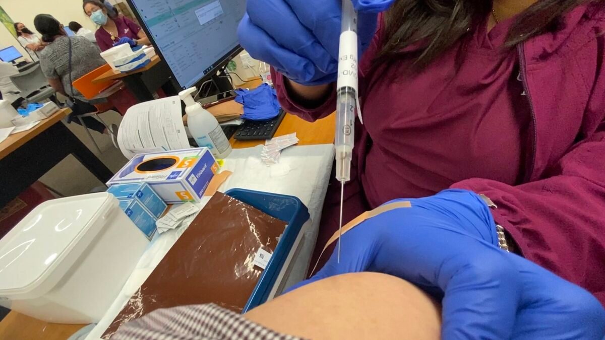 Injection d'un vaccin dans le bras d'une personne, dans un centre de vaccination